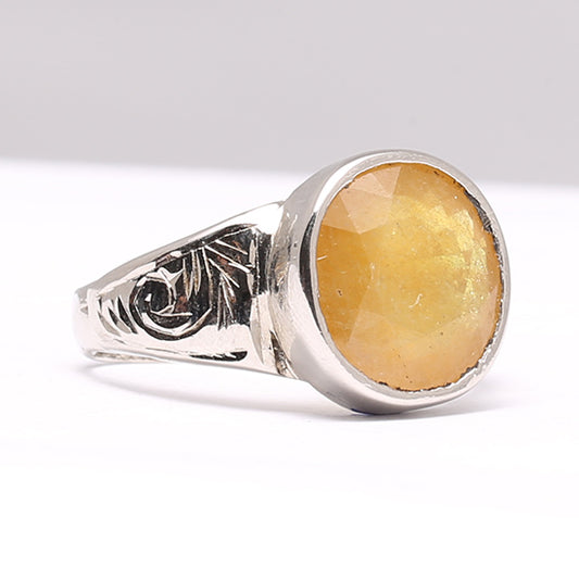 A silver ring with a yellow sapphire stone set in the center, surrounded by a decorative metal pattern.